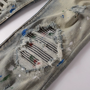 Macro detail of men's distressed slim jeans with paint splatters and denim patches