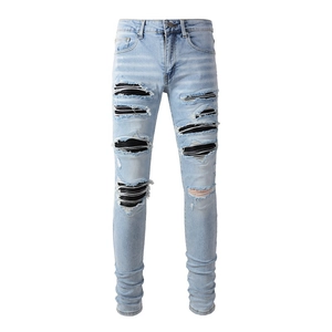 Detail of light blue slim jeans featuring heavy distressing and black striped inner patches