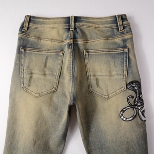 Détail du jean dégradé jaune-bleu avec broderie de serpent sur la poche arrière style rétro