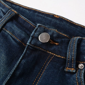 Détail d'un jean bleu pour homme avec bouton en métal argenté et surpiqûres dorées