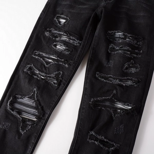 Detail of distressed black denim jeans with ripped holes and striped fabric backing