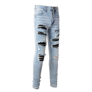 Detail of ripped light blue slim jeans with black accordion pleated leather patches