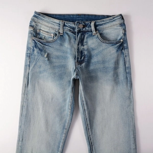 Detailed macro view of light blue washed denim jeans featuring worn distressed holes and seams