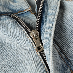 Detailed macro view of high-quality silver metal zipper and orange stitching on denim jeans