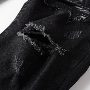 Close-up of distressed black denim fabric with heavy ripped details and frayed threads