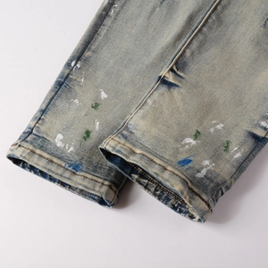 Close-up of distressed blue denim hem with artistic multi-color paint splatter detail