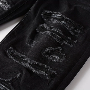 Close-up of heavy distressed details and ripped fibers on black slim denim jeans