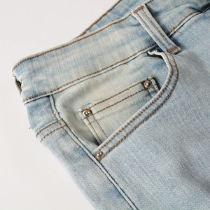 Detailed close-up of light blue denim jeans showing stitching, side pocket and metal rivets