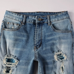 Detail of blue distressed denim jeans with sparkly sequin inserts in thigh rips