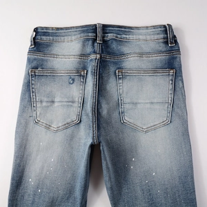 Detail of blue denim jeans featuring back pocket distressing and white paint splatter accents