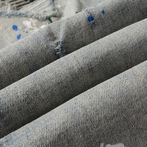 Detail of distressed light blue denim fabric with white paint splatters and worn texture