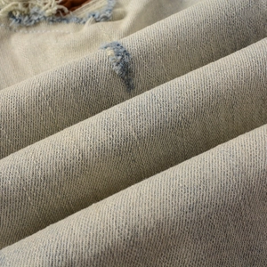 Vue macro du tissu denim beige clair avec texture sergée et détails vintage usés