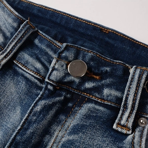 Close-up of distressed blue denim jeans showing metallic button and orange contrast stitching
