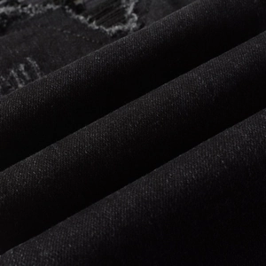 Macro view of black denim fabric texture with distressed ripped holes and fringe details