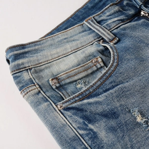 Detail of light blue denim jeans showing the waist, pocket, and vintage rivets