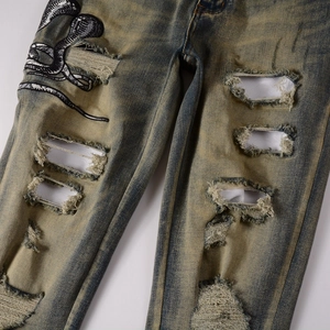 Détail du denim vintage délavé avec trous usés et broderie cobra sur le tissu