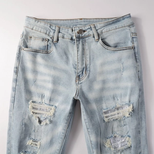 Detail of light blue washed denim jeans featuring distressed rips with sparkling rhinestones