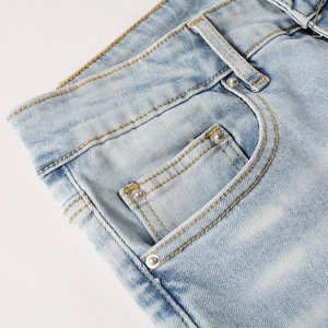 Detailed macro view of light blue denim waist, showing coin pocket and metal rivets