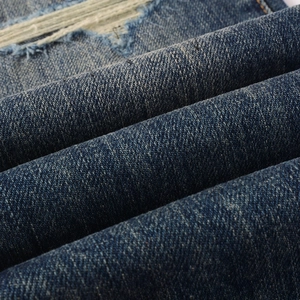 Detailed close-up of distressed denim fabric with authentic hand-grinding and white warp threads