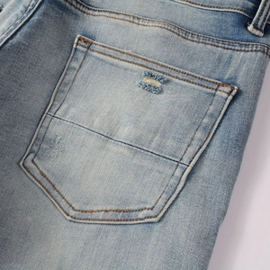 Detailed close-up of light blue denim jeans showing rear pocket with distressed rip detail