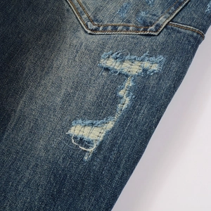 Close-up of blue denim jeans showing heavy distressed details and contrast yellow stitching