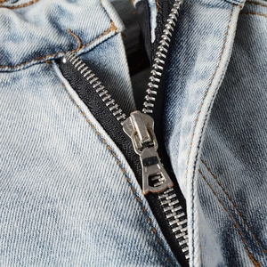 Detail of metal zipper and contrast stitching on light blue distressed denim jeans