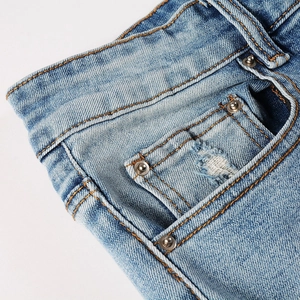 Close-up of light blue denim fabric featuring orange stitching and metal rivet details