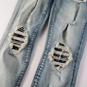 Detailed close-up of blue distressed jeans with bandana patchwork and white frayed stitching