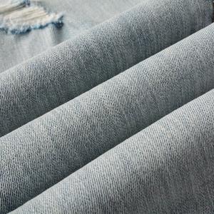 Close-up of light blue twill denim fabric with distressed ripped detail on slim fit jeans