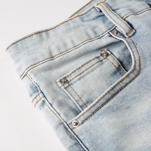 Detail of light blue denim waist with orange stitching and silver rivets on pockets