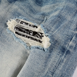 Close-up of acid wash blue denim with ripped details and black paisley patchwork lining