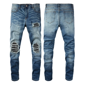Détail d'un jean bleu slim avec genoux déchirés et empiècements en patchwork de cuir noir
