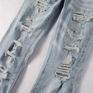 Close-up of distressed light blue jeans featuring heavy rhinestone embellishments and frayed holes