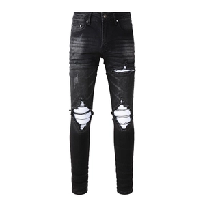 Detail of black distressed denim jeans with white horizontal stripe knee patches