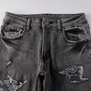 Close-up of distressed charcoal jeans with paisley fabric patches under ripped denim
