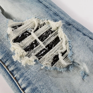 Macro view of light blue washed denim with distressed knee hole and paisley patch detail