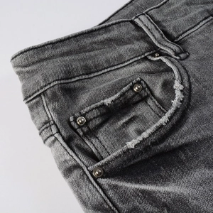 Detail of dark gray slim-fit jeans showing denim texture, rivets, and faded pocket whiskering