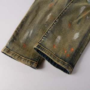 Detail einer Distressed-Jeans mit orangefarbenen Farbspritzern auf Vintage-Gelb gewaschenem Stoff