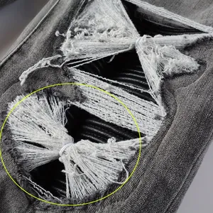 Détail macro d'un jean gris vieilli avec trous déchirés et empiècements en cuir PU noir