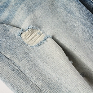 Close-up of distressed light blue denim jeans with ripped holes and beige woven fabric patch