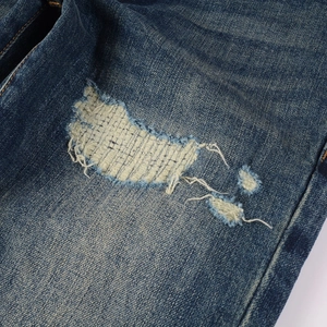 Macro shot of blue denim jeans featuring distressed rips and white reinforced stitching