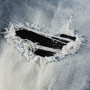 Detail of light blue washed denim with distressed rips and pleated black leather inserts