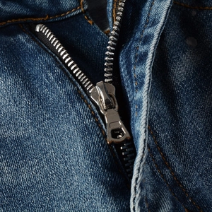 Macro della cerniera in argento e delle cuciture arancioni sui jeans slim fit blu