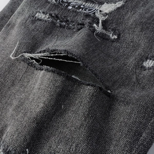 Close-up of distressed dark grey jeans with paisley patterned patchwork and frayed denim