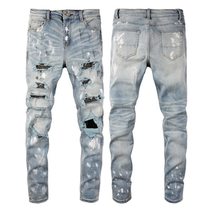 Detail of distressed blue jeans featuring rhinestone patches and white spray paint spray