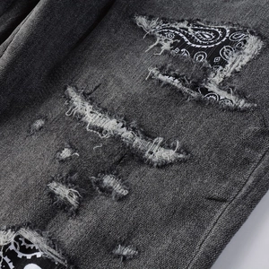 Detail of distressed dark grey denim with black paisley pattern patches and raw edges