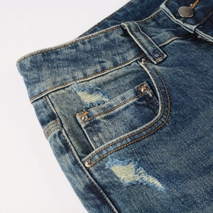 Close-up of distressed deep blue denim jeans showing vintage ripped pocket and metal button