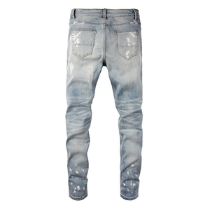 Detail view of light blue slim fit jeans with white paint splatter and distressed wash