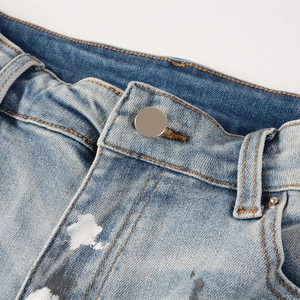 Detailed close-up of light blue denim jeans waist with white paint splatter and silver button