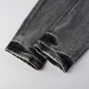 Detail view of dark grey denim pants featuring raw edge distressed cuffs and twill texture